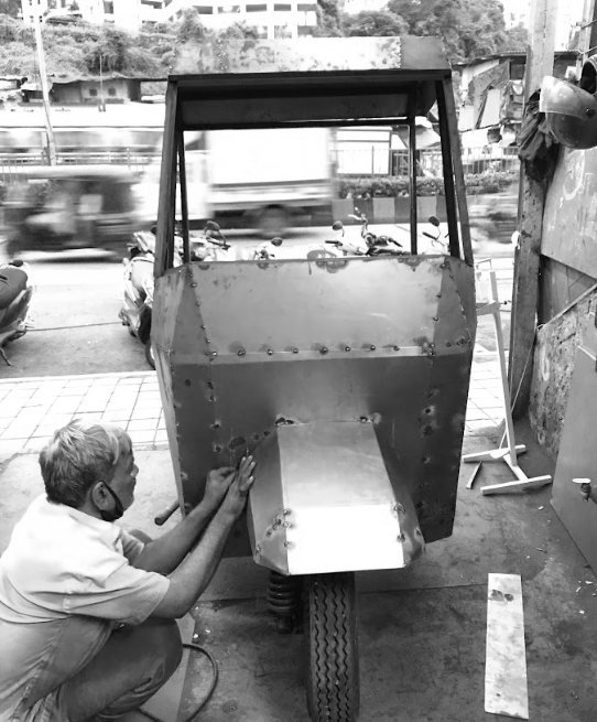 Black-and-white photo of the fabricator shaping the folded sheet-metal front of the cab