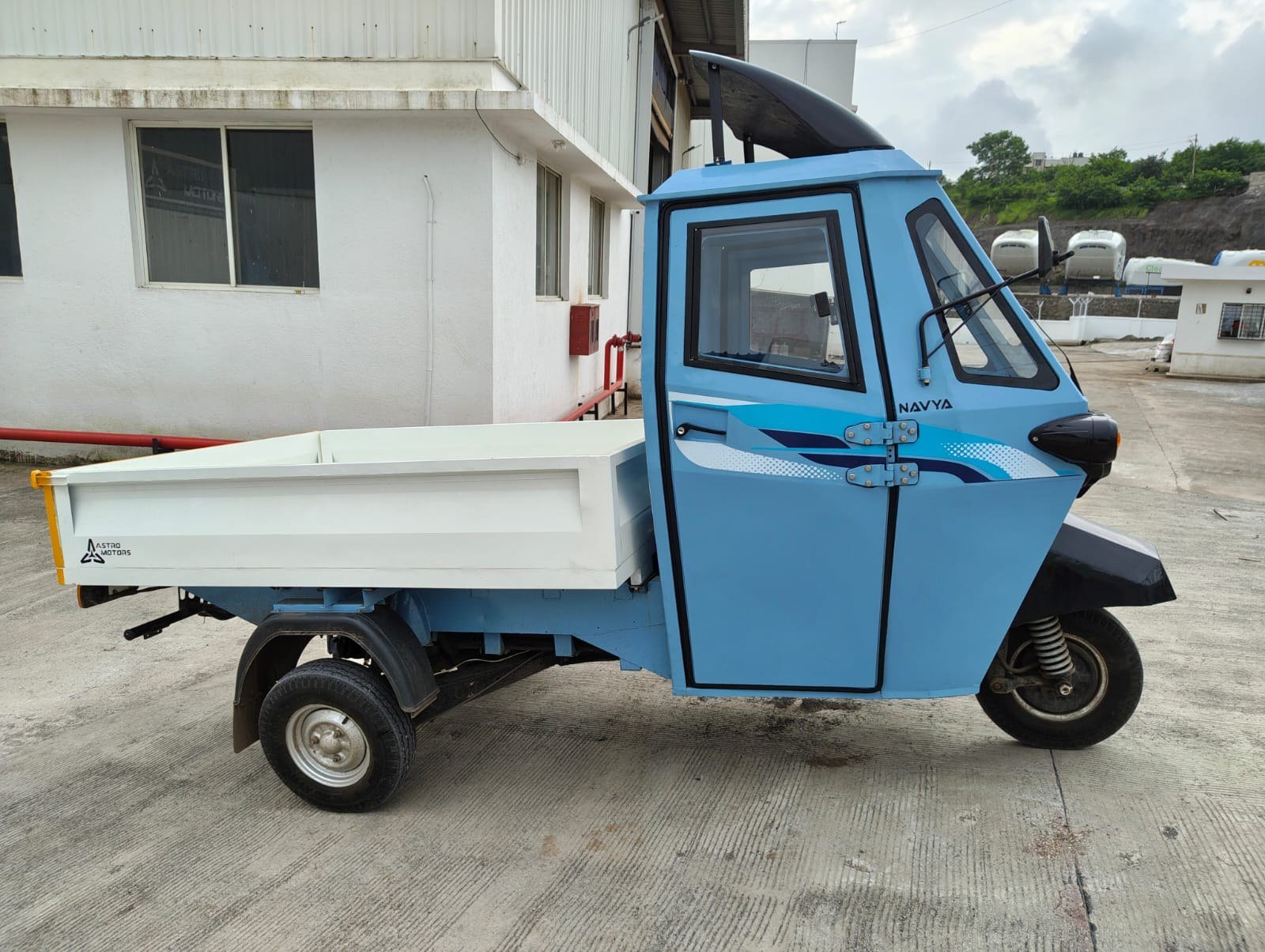 A painted blue Navya with white deck, parked outside the factory