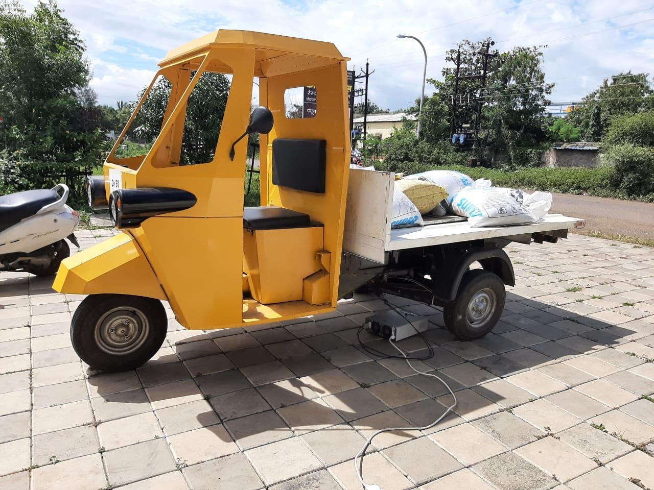 A yellow flatbed Navya parked outdoors with a load strapped on