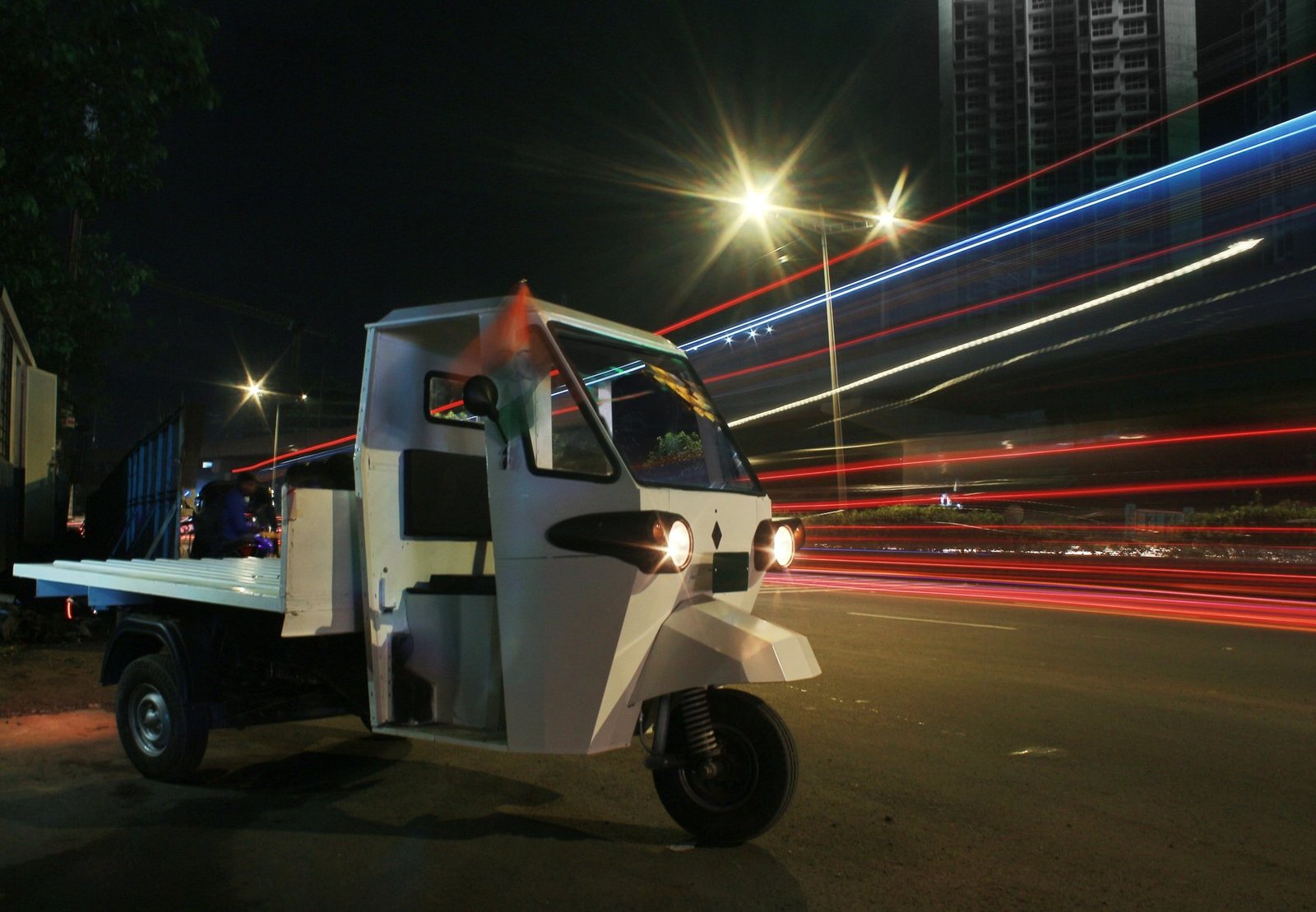 Navya electric cargo three-wheeler on a night road test, headlights on amid long light trails