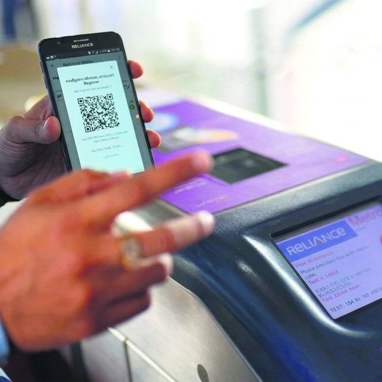 A commuter scanning a QR code from a phone at the Ridlr validator on a Mumbai Metro gate