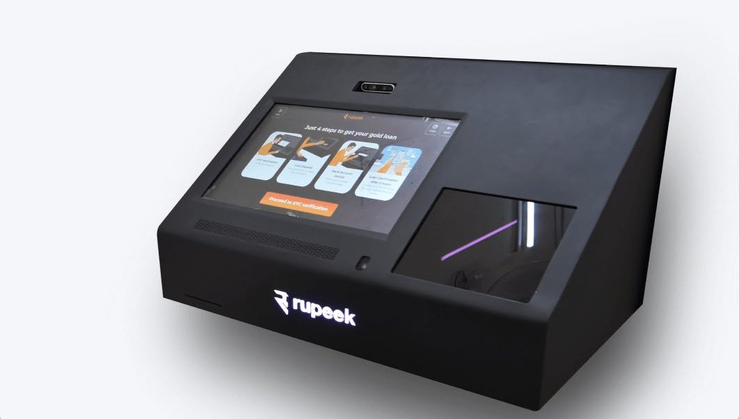 The Gold Teller Machine — a black desktop kiosk with an angled touchscreen, gold-deposit bay and glowing Rupeek wordmark